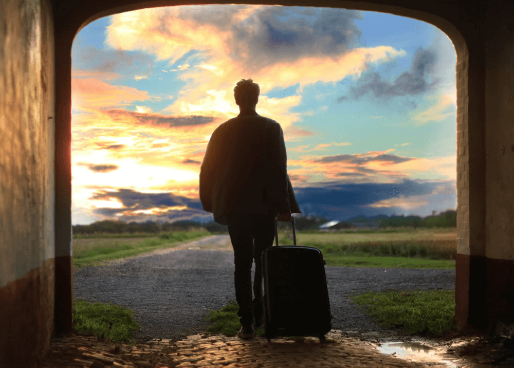 man looking down a road pulling a suitcase on wheels