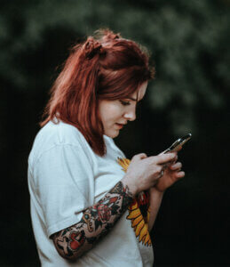 red-haired girl with tattoo sleeve using a cell phone