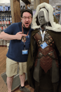 Man standing next to a full-sized figure of fantasy elf character in adventuring gear and cloak, Drizzt Do'Urden